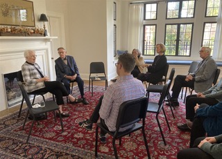 Guests seated in a circle of chairs for a talk in the Deanery's main room, beside the fireplace and bay windows